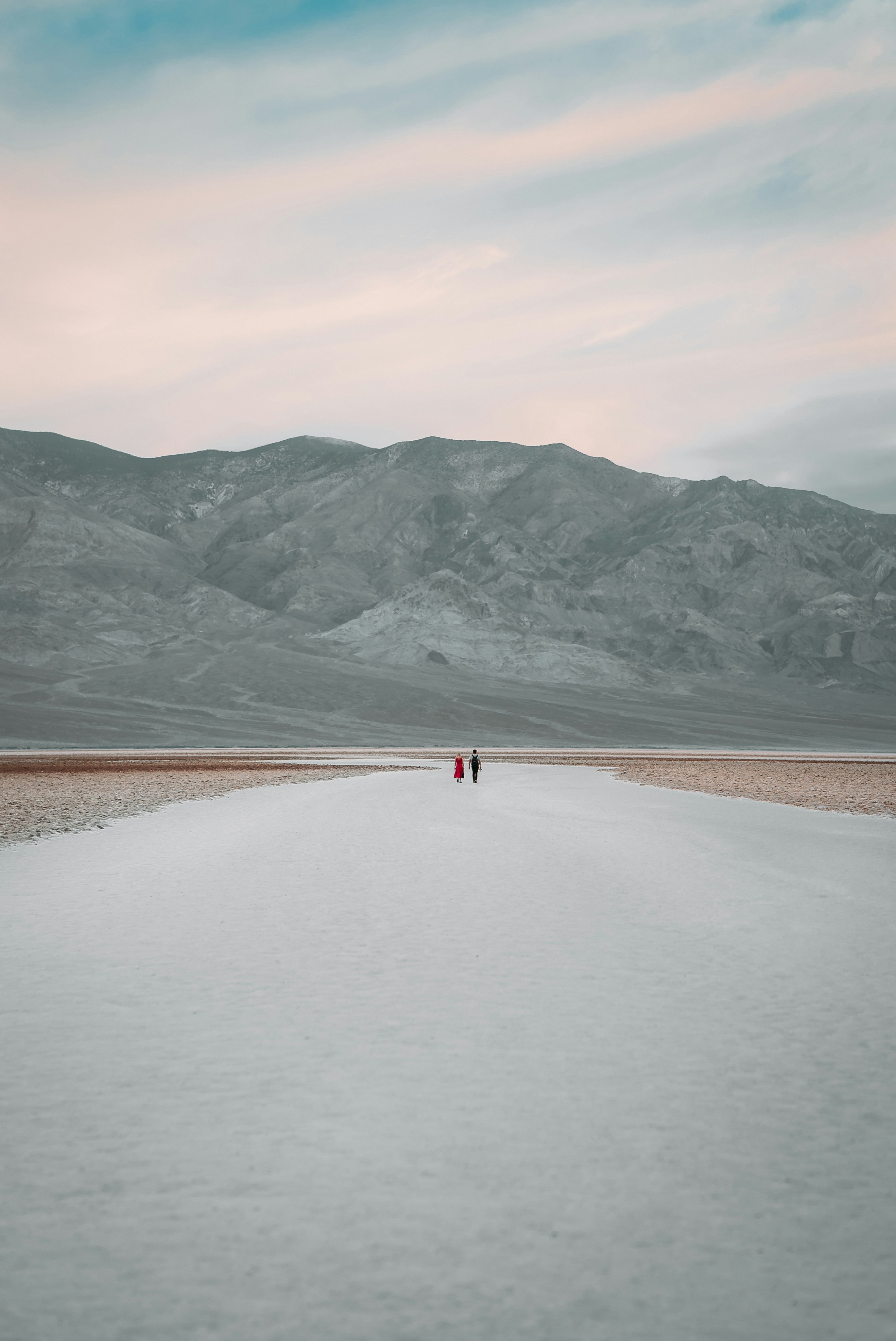 person walking on brown sand near lake and mountains during daytime